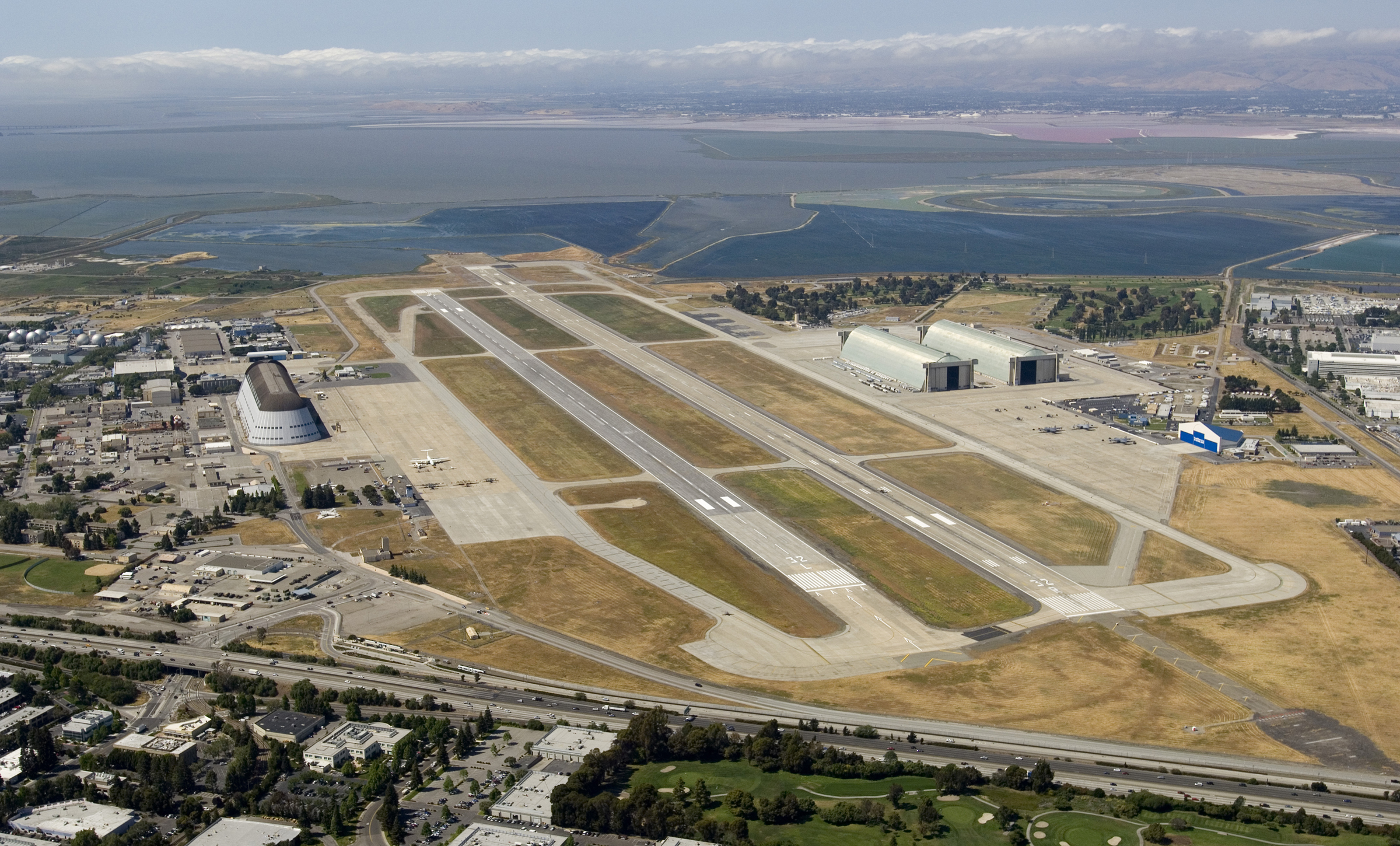 A birds-eye view of the Moffett Field runways. Hangar 1 is on the left. Hangars 2 and 3 are on the right. The San Francisco Bay is in the distance.