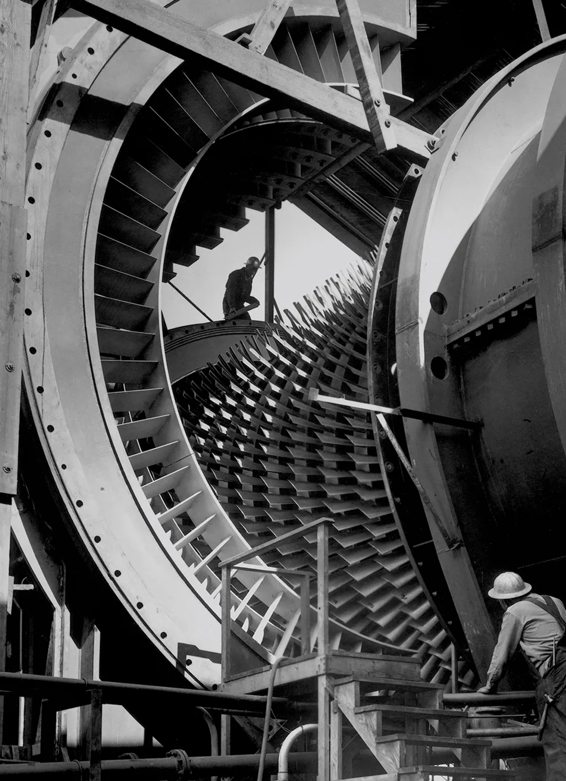 A man wearing a white hard hat examines a huge industrial machine made of large circular discs with short, tightly spaced, fanlike blades.