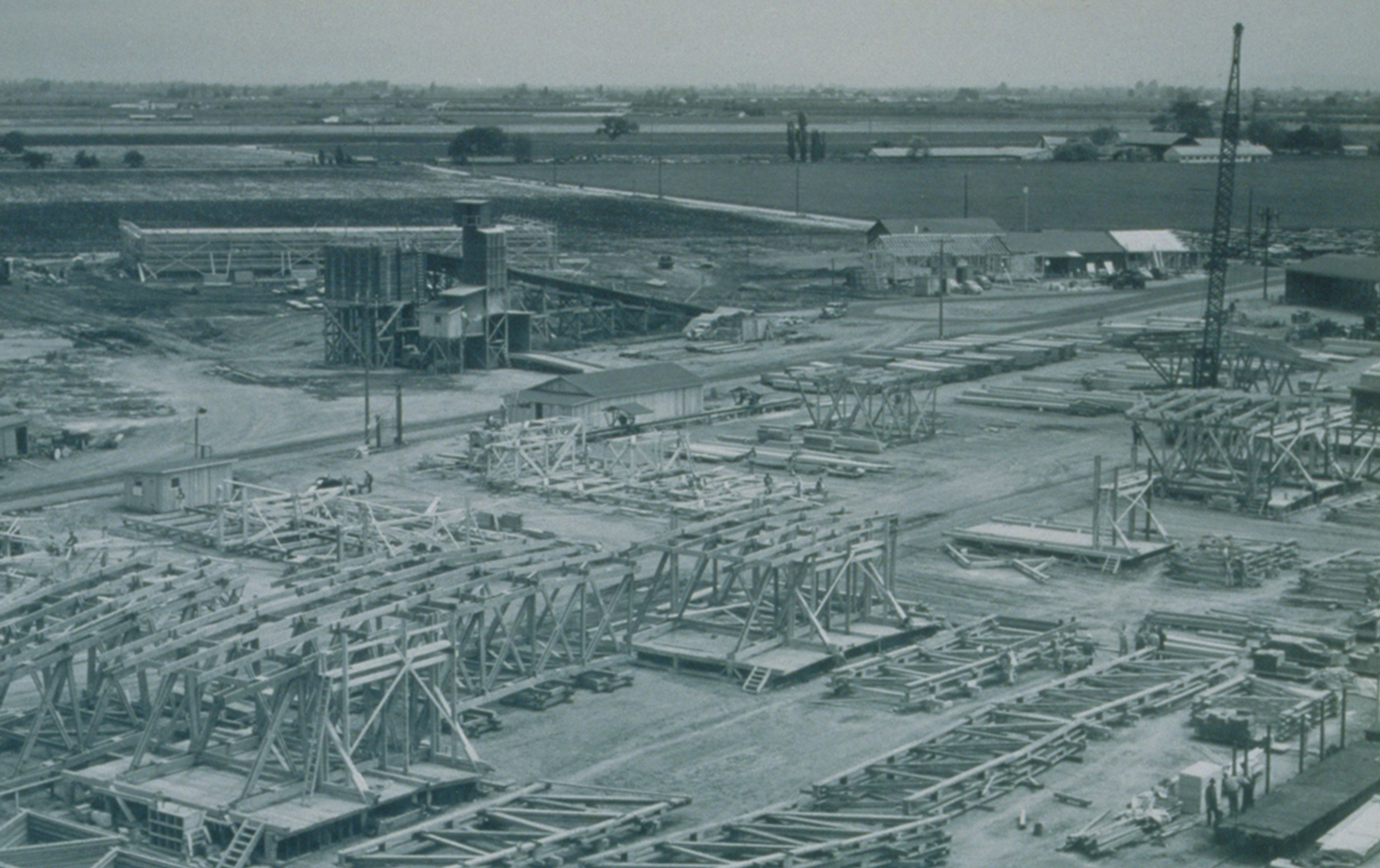 A birds-eye view of rows of dozens of large wood trusses being built onsite for the construction of 2 blimp hangars.
