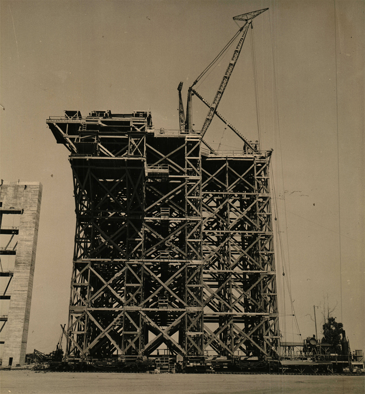 A tall and wide movable scaffolding tower with a construction crane on top used to assemble the wood trusses for Hangars 2 and 3.