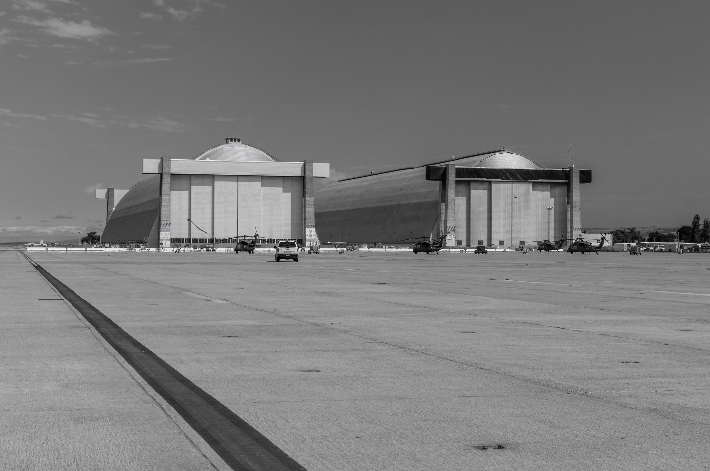 A wide view of Hangars 2 and 3 with a bold runway stripe on the left. A pickup truck and 4 rescue helicopters are parked near the hangar doors.